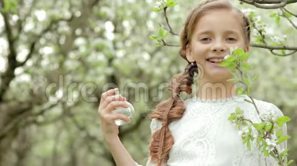 穿着白色连衣裙的辫子女孩嗅着瓶中的香水花枝在梨花园里缓慢地绽放视频的预览图