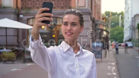美丽的现代女性站在街上白天在智能手机上自拍微笑交流理念视频的预览图