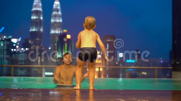 一个年轻人和他的小儿子在屋顶的游泳池里玩得很开心看到了摩天大楼视频的预览图