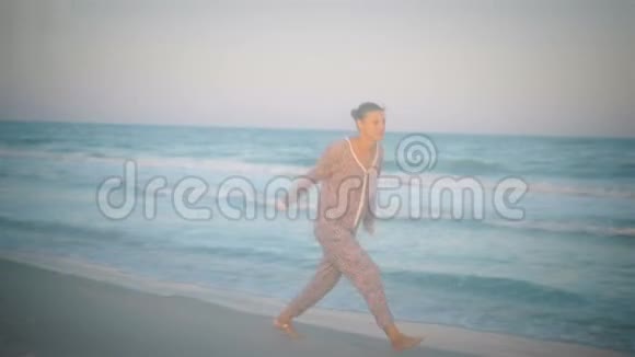 穿着睡衣的微笑女孩在风景如画的海边奔跑视频的预览图