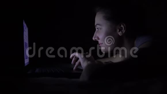 快乐的年轻女人躺在床上用笔记本电脑在黑暗的房间里4K视频的预览图