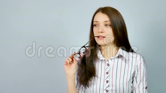 美丽的商务女性穿着衬衫戴着眼镜在工作室的灰色背景下微笑着看着视频的预览图