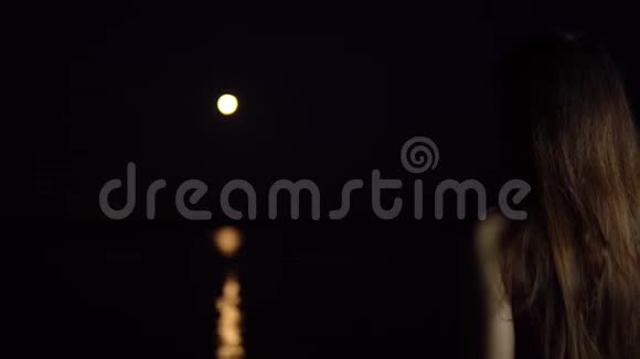 一个黑发的年轻女子欣赏河中倒影的红月视频的预览图