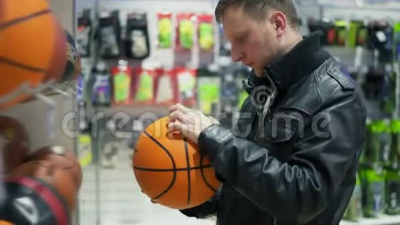 一个穿黑色皮夹克的成年男子检查了超市货架上的球一个男人看着视频的预览图