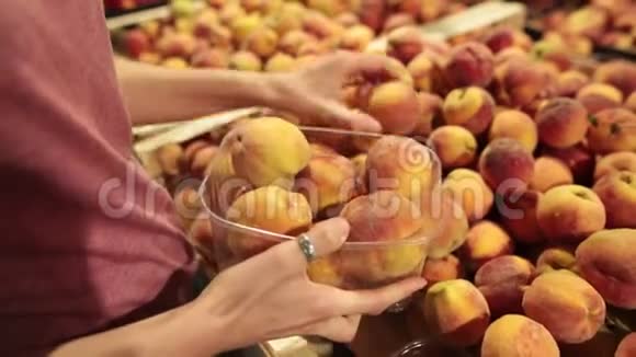 一个女人在商店柜台上选择桃子她把桃子放进一个塑料盒子里视频的预览图