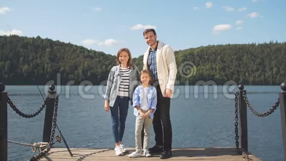 幸福的一家人在安静的湖边摆姿势时看着摄像机视频的预览图