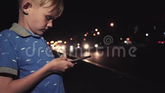 小男孩晚上在城里玩手机视频的预览图
