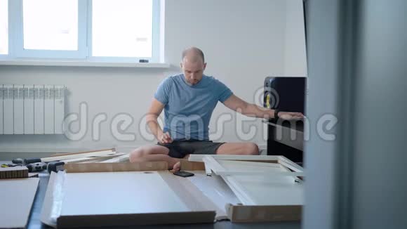 年轻人正在整理和探索新家具的部分坐在他那清澈的公寓的地板上视频的预览图