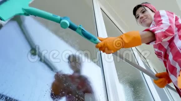 在窗户里玻璃反射着微笑的白种人美丽的女人戴着手套用特殊的拖把清洗窗户视频的预览图
