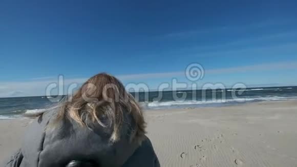 可爱的金发女孩踩在沙滩上背景是蓝色的海浪蓝天视频的预览图