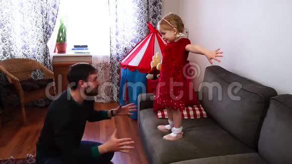 小女孩从沙发上跳了下来爸爸用手抓住他的女儿视频的预览图