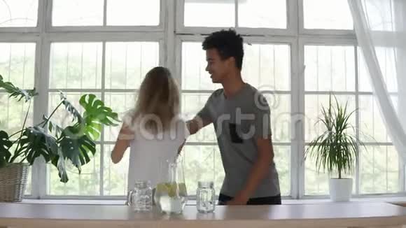 漂亮的非洲男人在厨房跳舞时拥抱他的高加索女朋友一对穿着睡衣的夫妇视频的预览图
