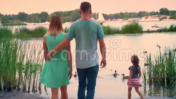 年轻家庭的剪影是夏天在公园里散步日落在湖上看鸭子大自然的概念视频的预览图
