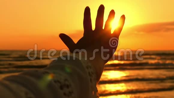 一位年轻女子的手在海上日落的背景下缓缓地抬起抚摸着阳光视频的预览图