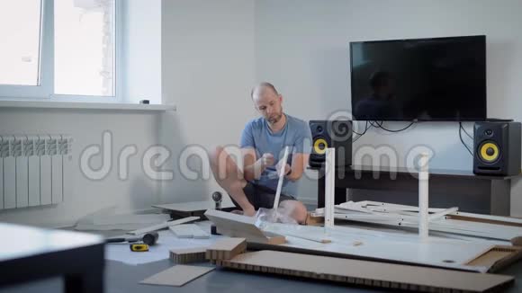 一个人正在组装一个新的家具安装零件并将其固定在一个明亮的家庭细节和工具的房间里视频的预览图