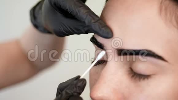 特写镜头身穿黑色橡胶手套的美容师的手拿着棉签纠正眉毛的形状视频的预览图