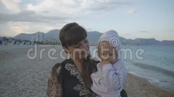 年轻的母亲带着孩子在日落海滩上漂亮的白种人穿着黑色紧身连衣裙两岁走路视频的预览图