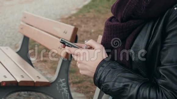 在公园里用智能手机坐在长凳上合上女人的手美丽的欧洲女孩打电话发短信视频的预览图