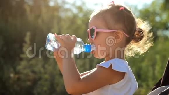 戴太阳镜的女孩子从瓶子里喝水阳光明媚的一天儿童肖像特写视频的预览图