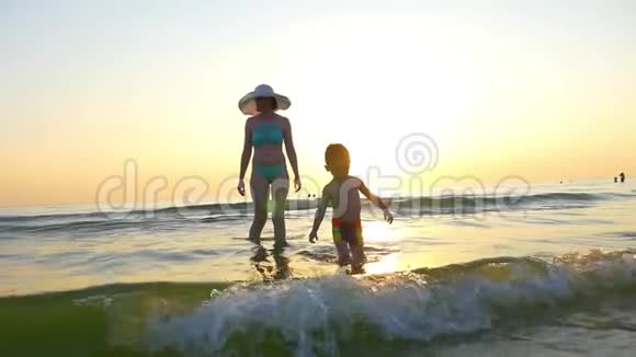 快乐的小男孩和他的母亲一起走在海边的沙滩上一个幸福的家庭踏着海浪视频的预览图