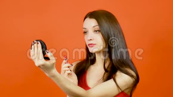 红顶美女肖像工作室用鲜艳的口红和橙色背景上的小镜子视频的预览图