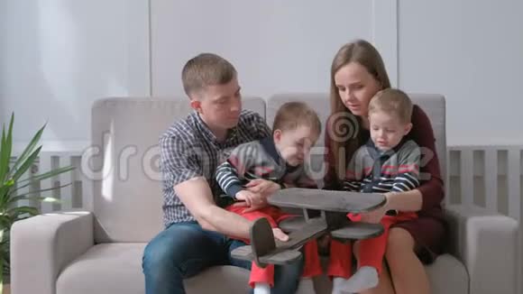 一家人的爸爸妈妈和两个双胞胎兄弟坐在沙发上玩木飞机视频的预览图