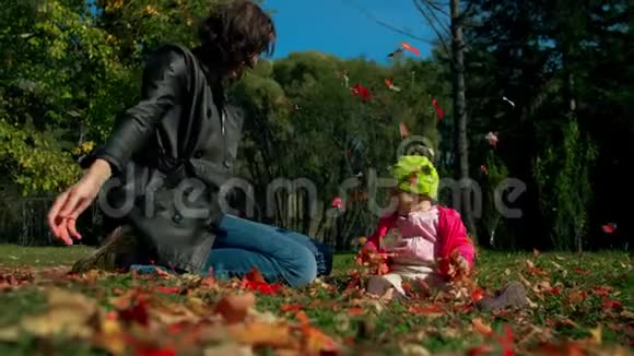 妈妈和女儿坐在秋天的草地上玩着落下来的红黄叶视频的预览图