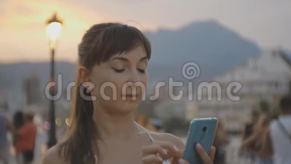 漂亮的年轻女性有智能手机微笑的白种人女人在夏日夕阳胜地的手机上聊天视频的预览图