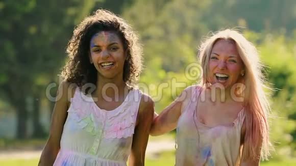 两个美丽的女孩涂满了颜料微笑着在色彩节上摆姿势拍照视频的预览图