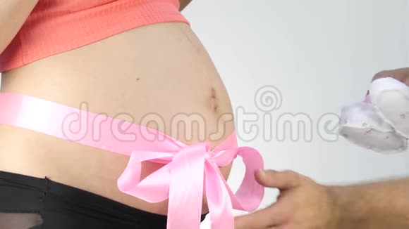 男人手在玩婴儿鞋怀孕的腹部有粉红色的丝带4K视频的预览图