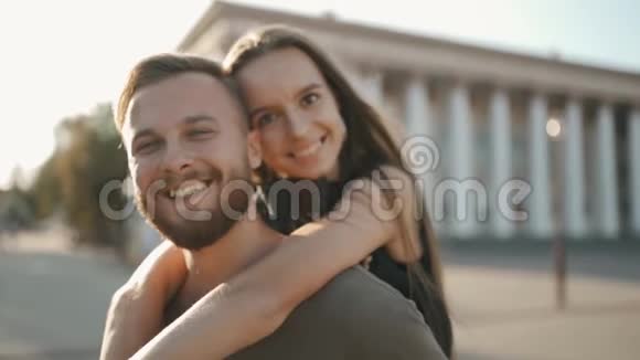 爱你一个女孩在一个男人的肩膀上一起看着相机在夕阳的背面微笑视频的预览图