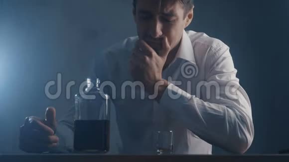 沮丧的商人把威士忌倒在一个玻璃杯里独自在黑暗的房间里喝酒酗酒的概念视频的预览图