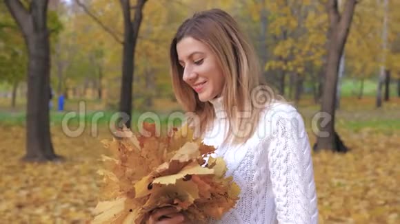 秋天公园里女人抱着黄色落叶的花团视频的预览图
