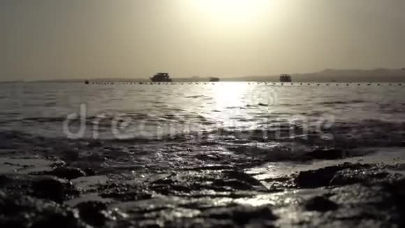 海浪在日落时冲刷着海岸和背景帆船视频的预览图