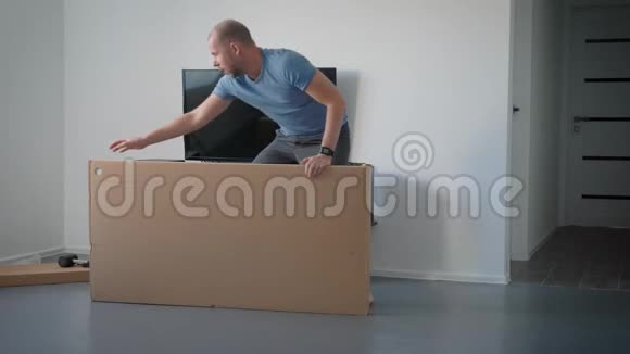 成年男子正在公寓的一个房间里翻来覆去地躺在一个大纸板箱上剪着包装胶带视频的预览图