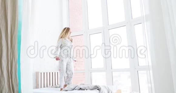 年轻迷人的金发女郎穿着睡衣在卧室的床上跳舞视频的预览图