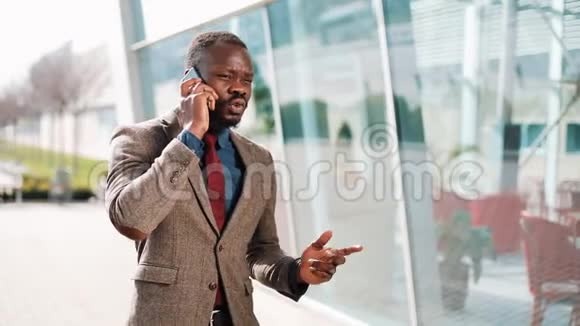 年轻的非裔美国商人站在现代办公室旁边谈论他的智能手机他在谈他的生意视频的预览图