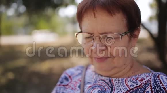 公园里戴眼镜的老妇人坐在长凳上看一本电子书视频的预览图