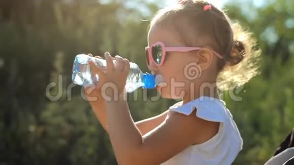 戴太阳镜的小女孩从瓶子里喝水在阳光明媚的日子给孩子画特写视频的预览图