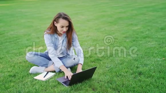 快乐的女人在夏天公园的绿色草坪上工作视频的预览图