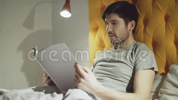 年轻的父亲看书而他的小儿子在晚上睡觉前跳上床视频的预览图