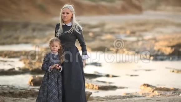 小女孩和她的母亲在大海背景下的日落时分穿着贵族的老式服装视频的预览图