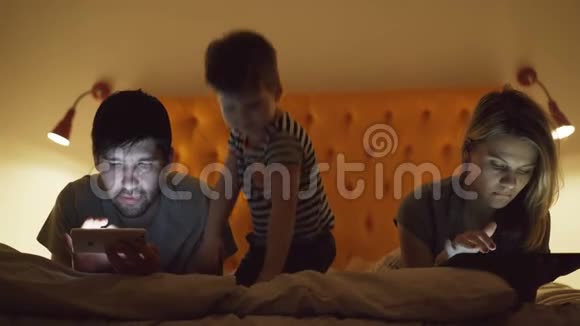 幸福的家庭小儿子躺在床上用平板电脑和智能手机看电影和卡通视频的预览图