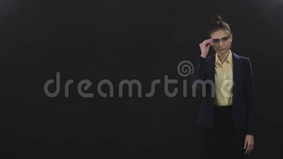 穿商务西装的聪明女士站在黑色背景上看着相机视频的预览图