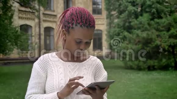 年轻的非洲裔美国妇女带着粉红色的可怕的袜子在平板电脑上打字坐在大学附近的公园里视频的预览图