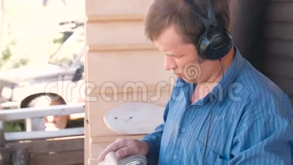木匠在磨床上打磨玩具车的木制部件在耳机里听音乐视频的预览图