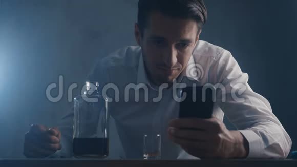 沮丧的商人把威士忌倒在一个玻璃杯里独自在黑暗的房间里喝酒酗酒的概念视频的预览图
