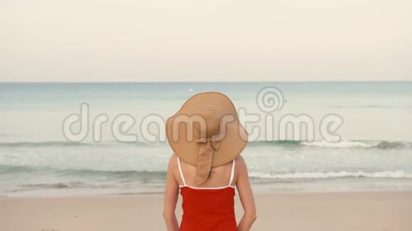 快乐的女旅行者穿着红色泳衣和帽子双手举起在完美的海滩上快乐视频的预览图