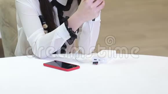 一个女孩坐在一张白色的桌子旁手里拿着一部从便携式充电器充电的手机视频的预览图