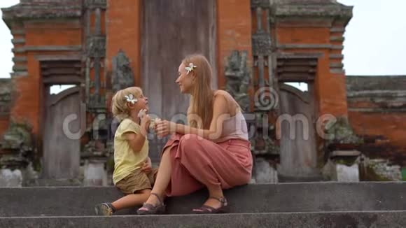 一名年轻女子和她的儿子坐在巴厘岛的塔曼阿云寺的楼梯上视频的预览图